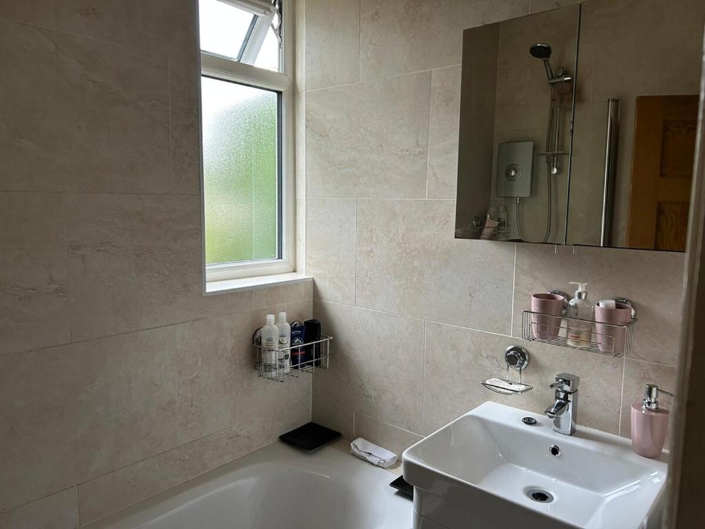 La salle de bains est pourvue d'un lavabo, d'une baignoire et d'une fenêtre. dans l'établissement Cosy 3 bedroom house to rent, à Manchester