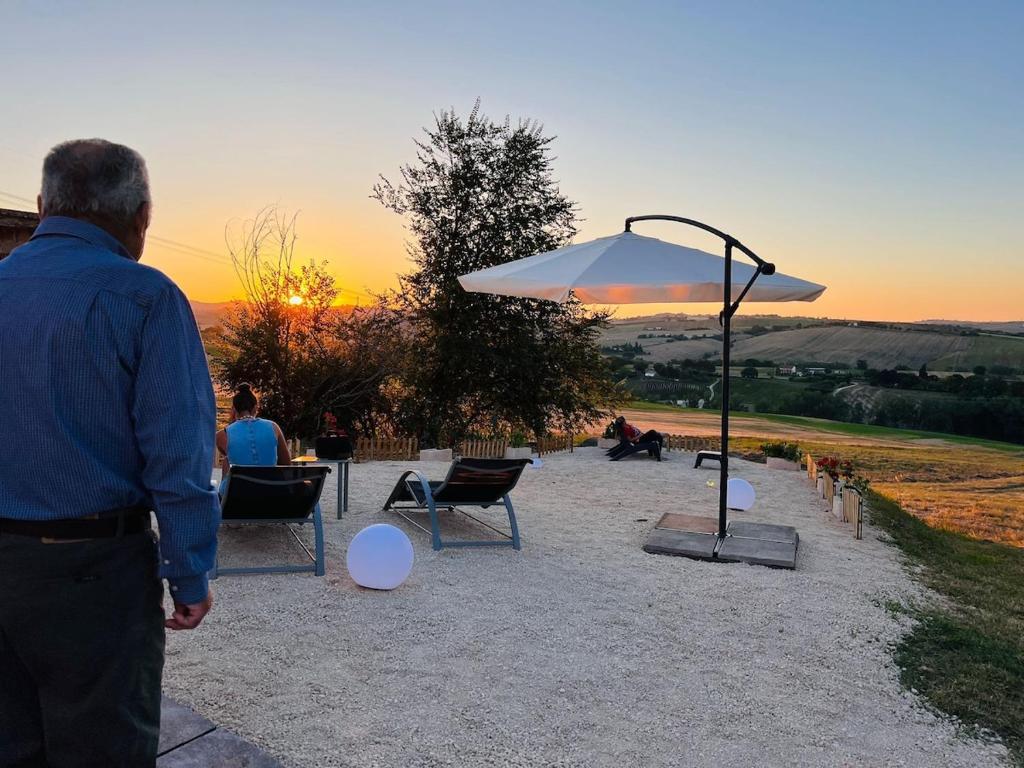a man standing in front of a table and an umbrella at Casale Nonno Dario, Balcone delle Marche Cingoli in Troviggiano