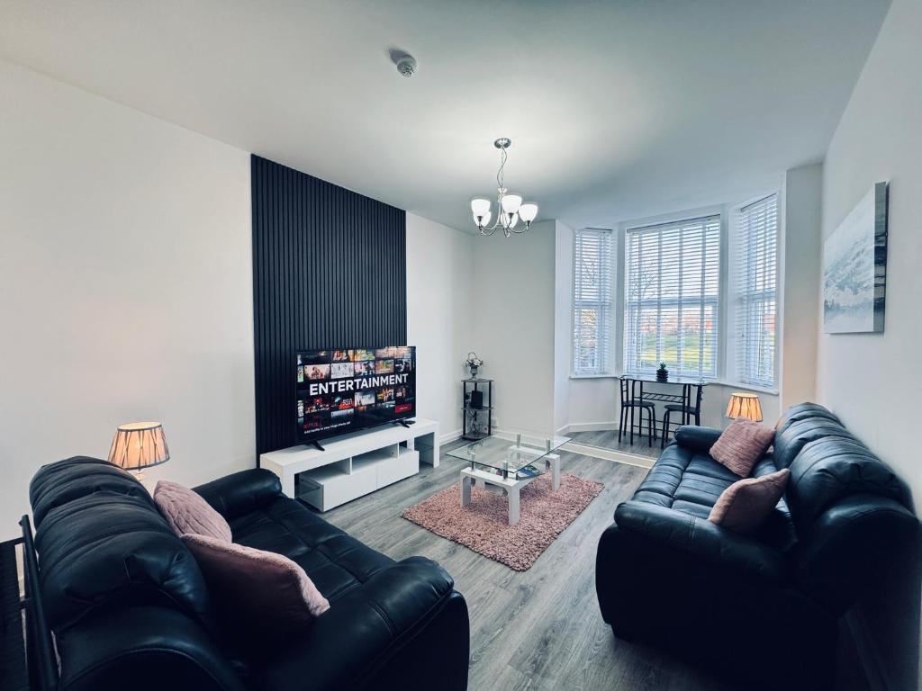 a living room with a black leather couch and a tv at Spanish City View 1, Stylish Sea Front Apartment Free Onsite Parking in Whitley Bay
