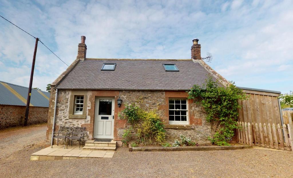 a stone cottage with a white door and a fence at Mrs Moll's Cottage in Earlston