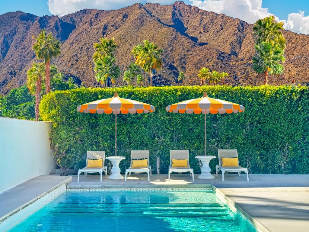 a pool with chairs and umbrellas and palm trees at Villa Caliente in Palm Springs