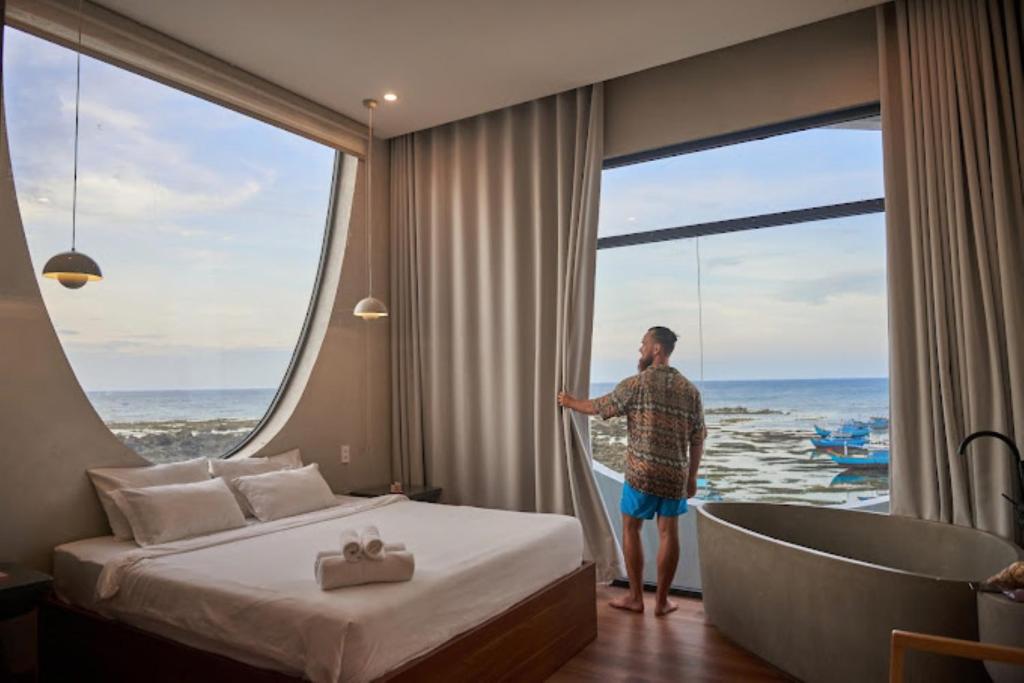 un homme debout dans une chambre d'hôtel regardant par la fenêtre dans l'établissement L'amant Boutiqué House Phú Quý, à Cu Lao Thu