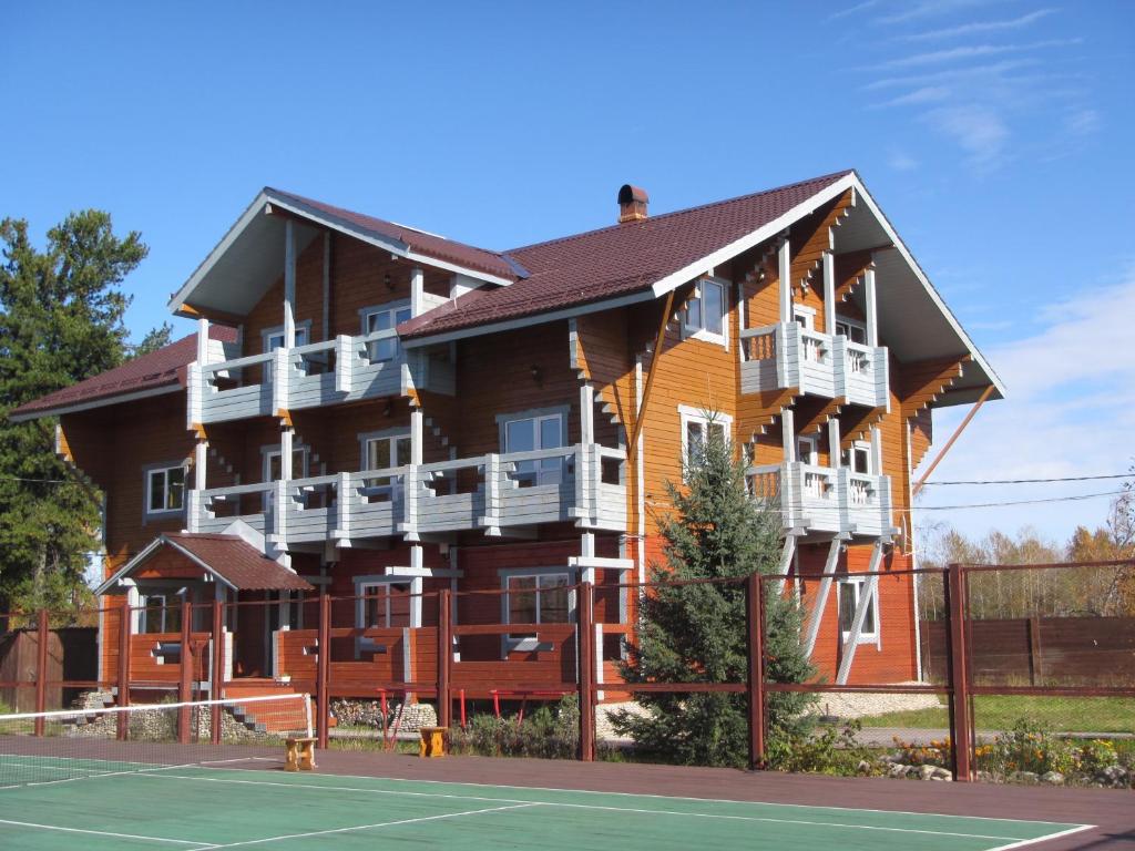 un gran edificio de madera con una pista de tenis delante de él en Usadba Novosnezhka, en Novosnezhnaya
