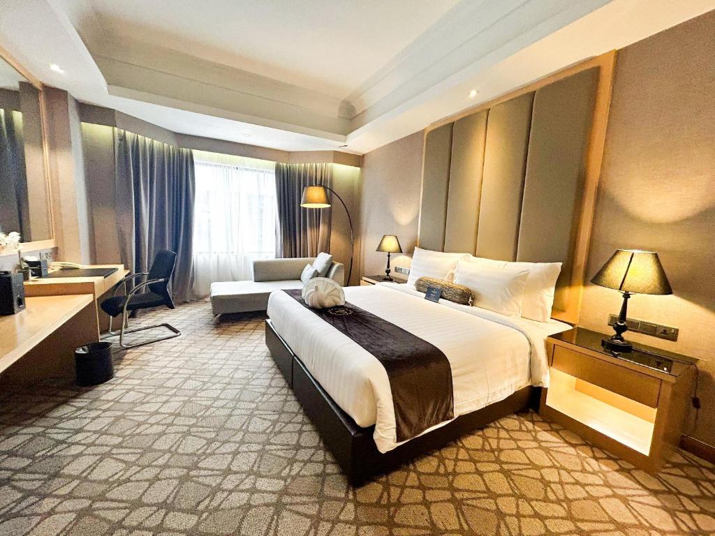 A king room with a large bed, desk, sofa, and curtained window.