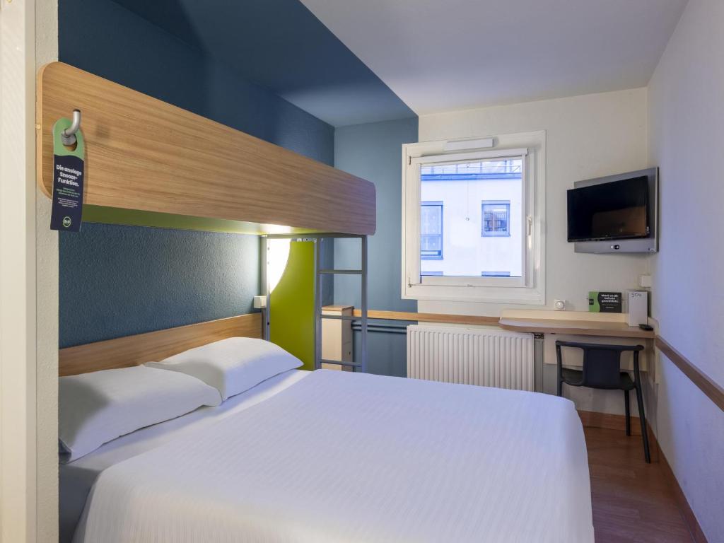 a bedroom with a bed and a desk and a window at B&B HOTEL Dortmund-Airport in Holzwickede