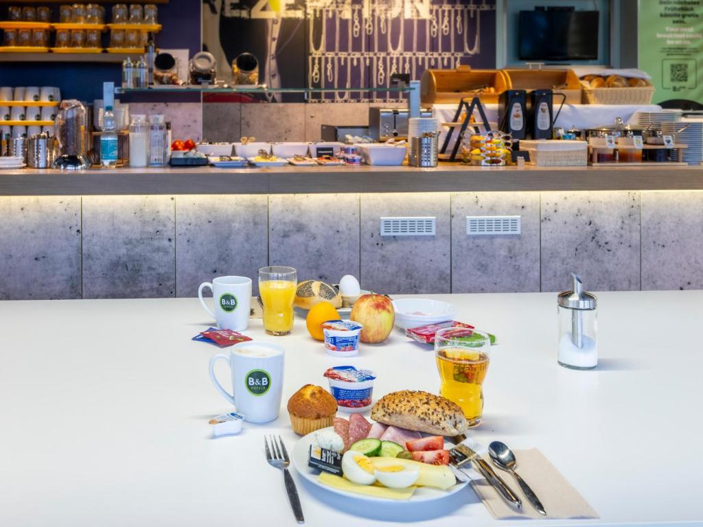 a table with a plate of food and drinks at B&B HOTEL Dortmund-Airport in Holzwickede