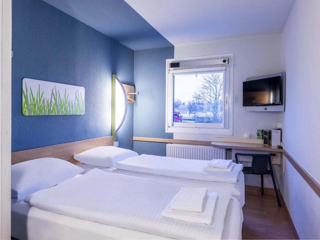 two beds in a room with a desk and a window at B&B HOTEL Dortmund-Airport in Holzwickede