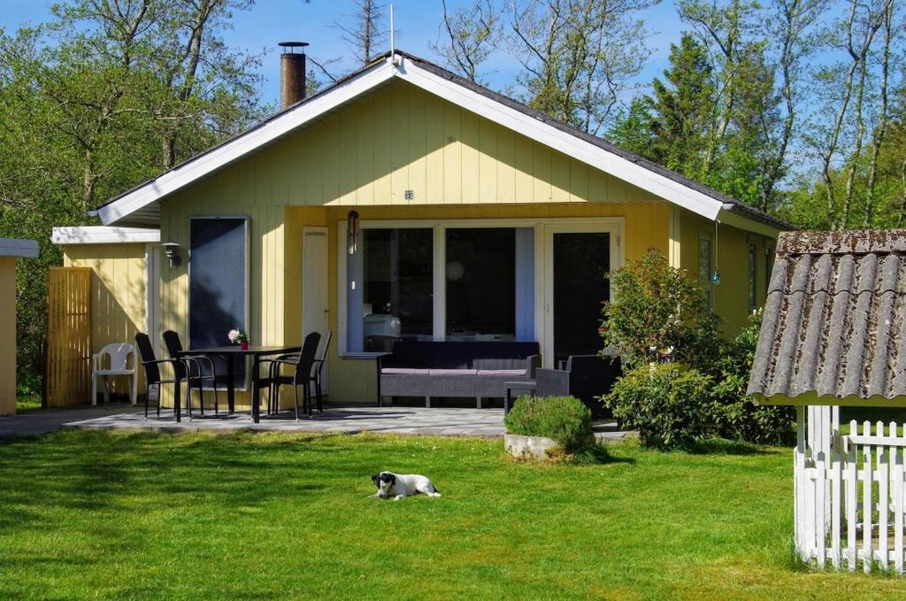 a small yellow house with a dog laying in the grass at Holiday Home in Thyholm