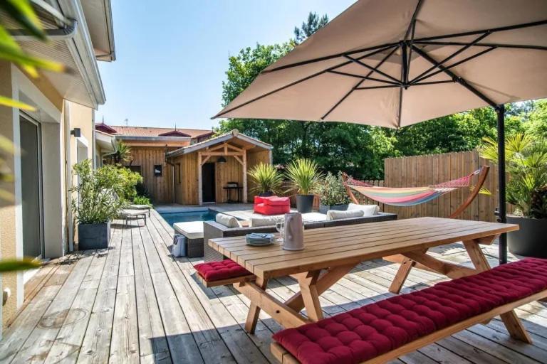 une terrasse en bois avec une table en bois et un parasol dans l'établissement Villa au charme familial avec belle terrasse et piscine chauffée, à La Teste-de-Buch