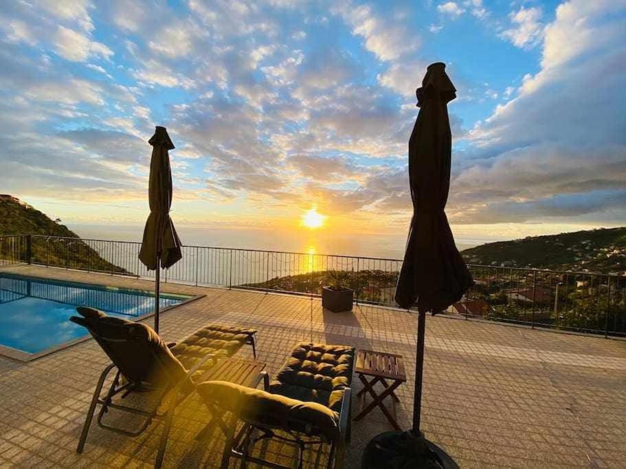 two umbrellas and chairs on a balcony with the sunset at Shangri Sol - Holiday house in Arco da Calheta