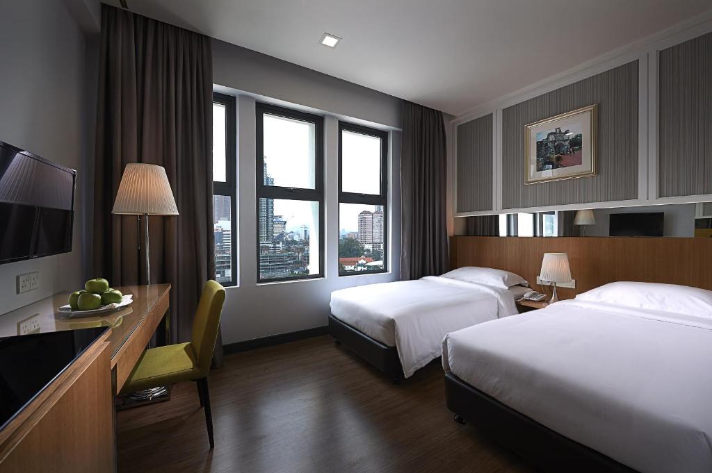 a hotel room with two beds and a desk at Hotel Transit Kuala Lumpur in Kuala Lumpur