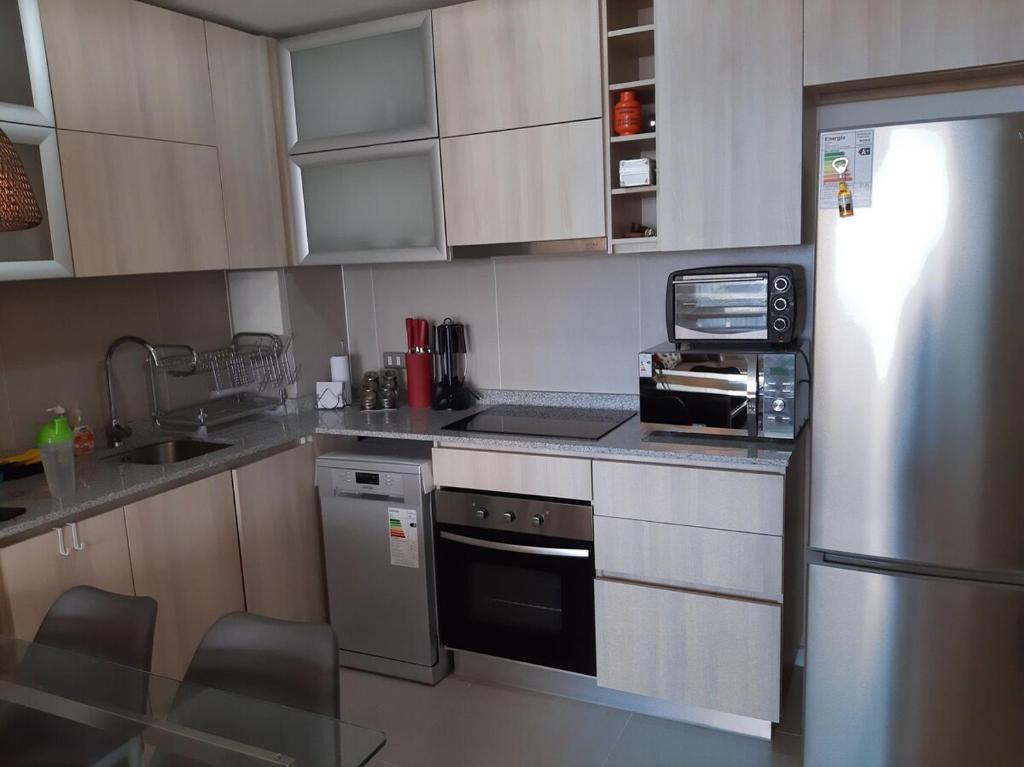Una cocina con gabinetes blancos y un refrigerador de acero inoxidable. en Depto Condominio Laguna Mar, en Las Cruces