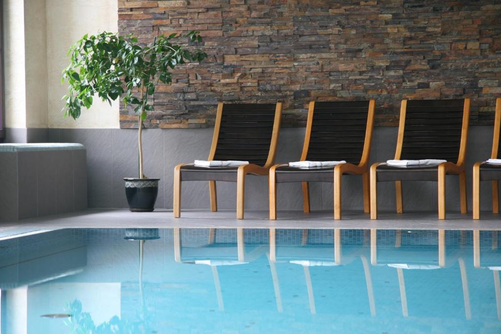 Row of wooden lounge chairs beside indoor pool, potted plant and stone accent wall reflected.