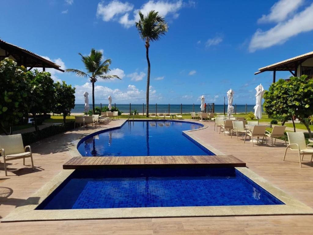 ein Pool in einem Resort mit Stühlen und Palmen in der Unterkunft Village Itacimirim Boulevard - Pé na areia in Itacimirim