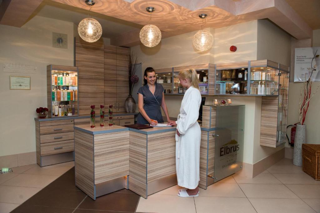 Spa receptionist assisting a guest in a white robe at a modern wooden reception counter.