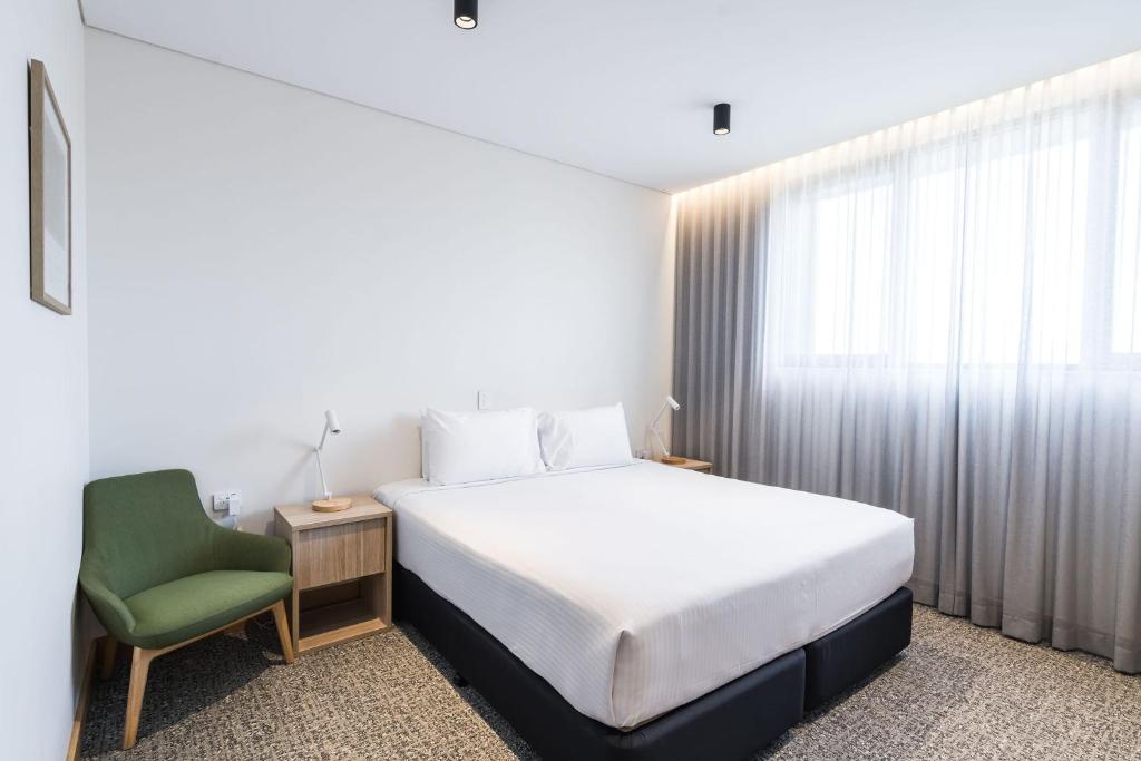 a bedroom with a white bed and a green chair at Mary MacKillop Place in Sydney