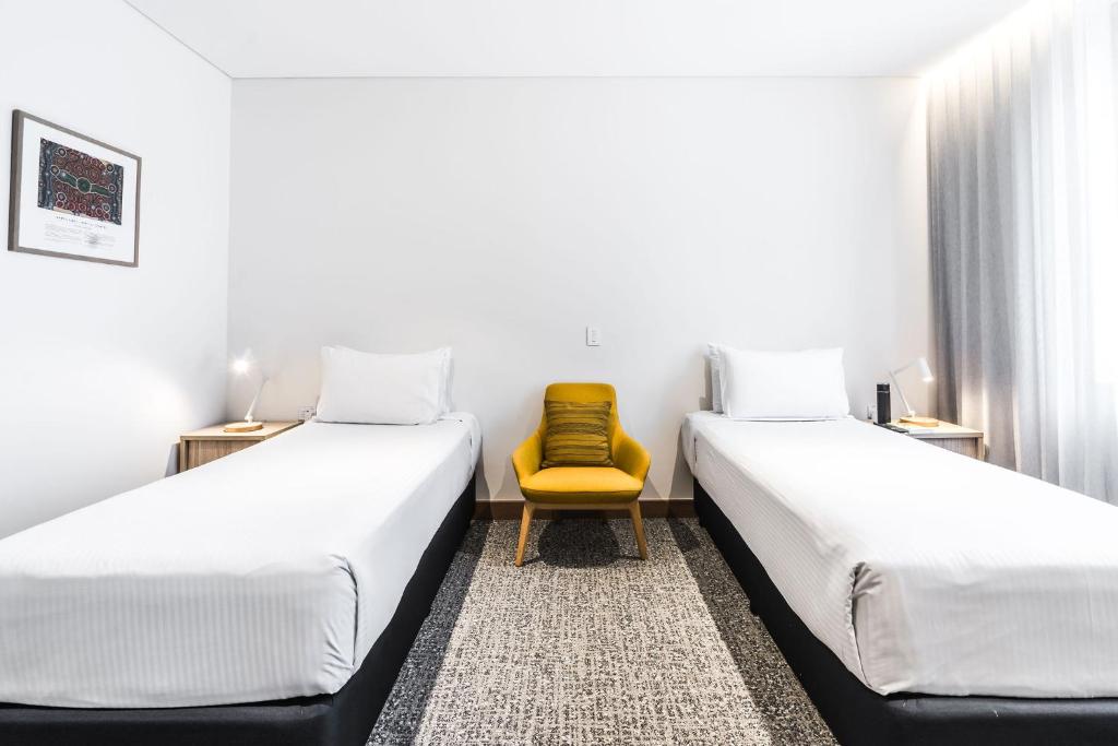 two beds in a room with a yellow chair at Mary MacKillop Place in Sydney