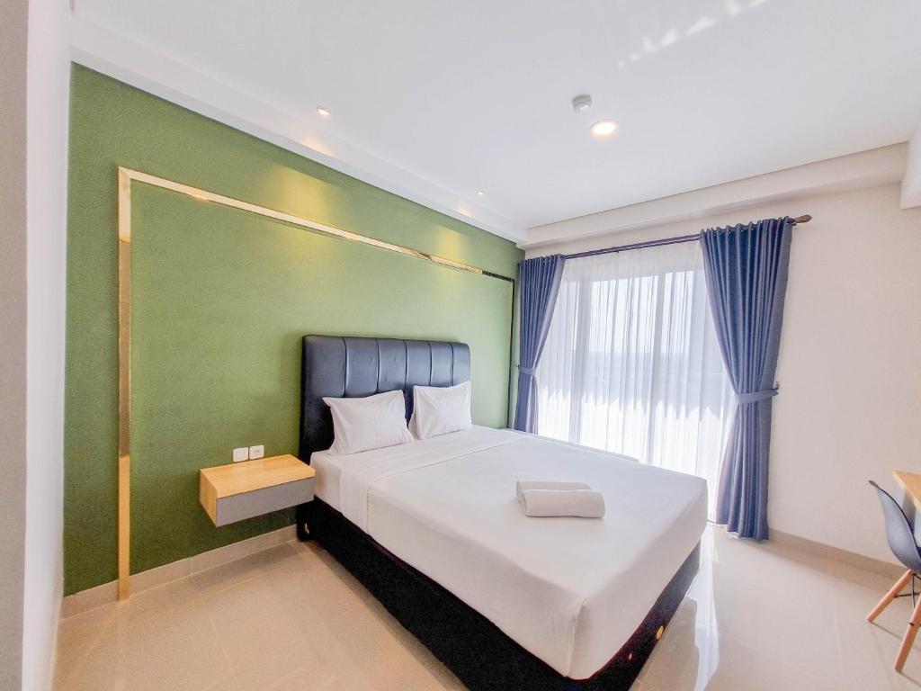 a bedroom with a large bed and a green wall at Homey and Minimalist Studio at Patraland Amarta Apartment By Travelio in Kejayan