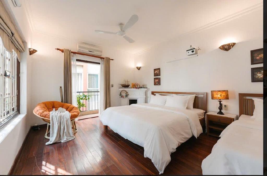 a white bedroom with two beds and a chair at Going Merry in Hanoi