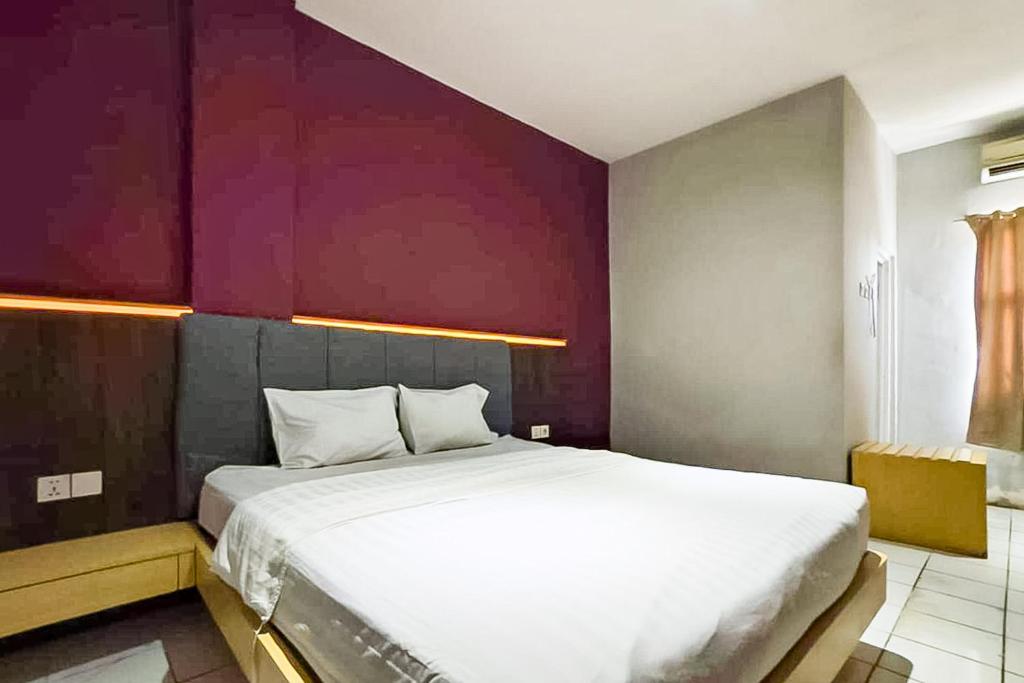 a bedroom with a large white bed with a purple wall at Hotel Ciputat RedPartner in Ciputat