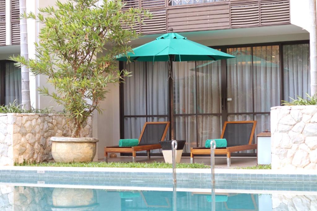 A swimming pool beside two loungers, a turquoise umbrella and ground-floor rooms.