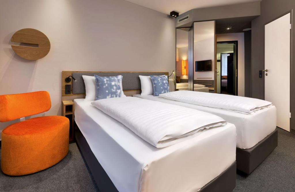two beds in a room with a chair and a bedroom at Flemings Express Hotel Frankfurt in Frankfurt