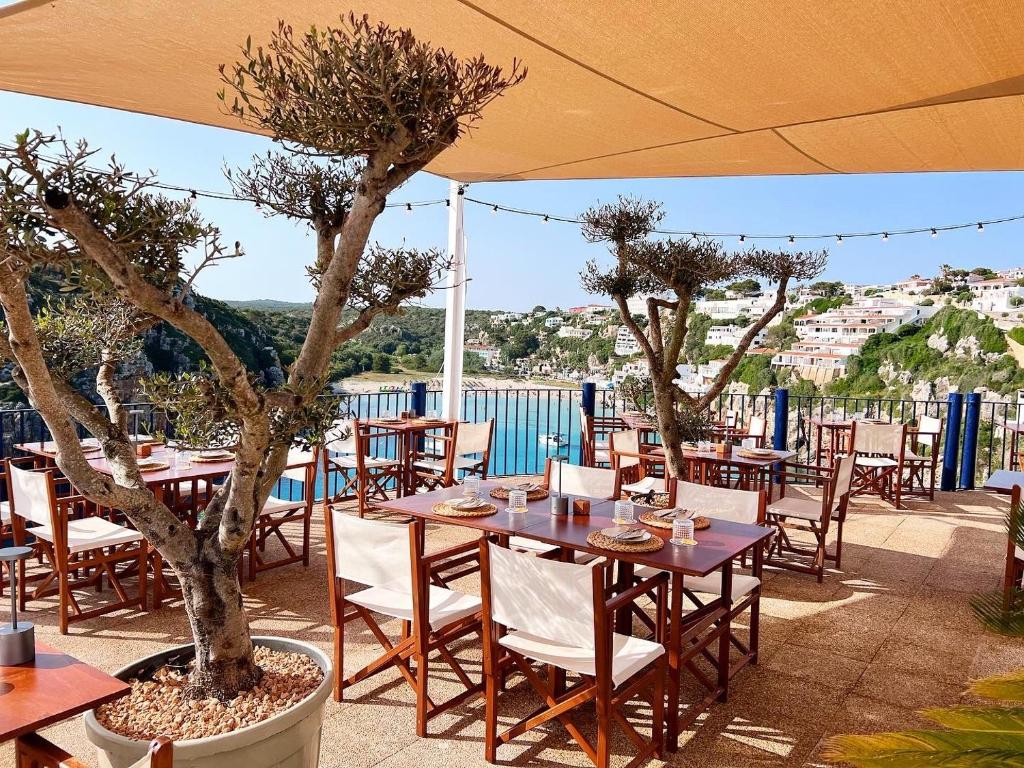a restaurant with tables and chairs and trees on a patio at Club Menorca - Solo Adultos in Cala'n Porter