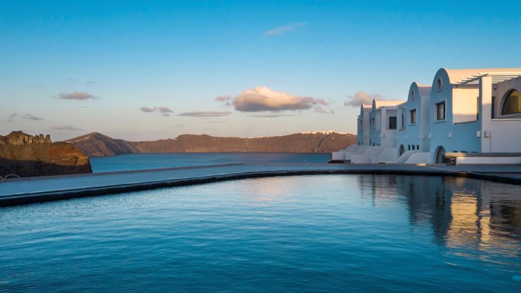 a pool of water with buildings and mountains in the background at The Duchess in Therasia