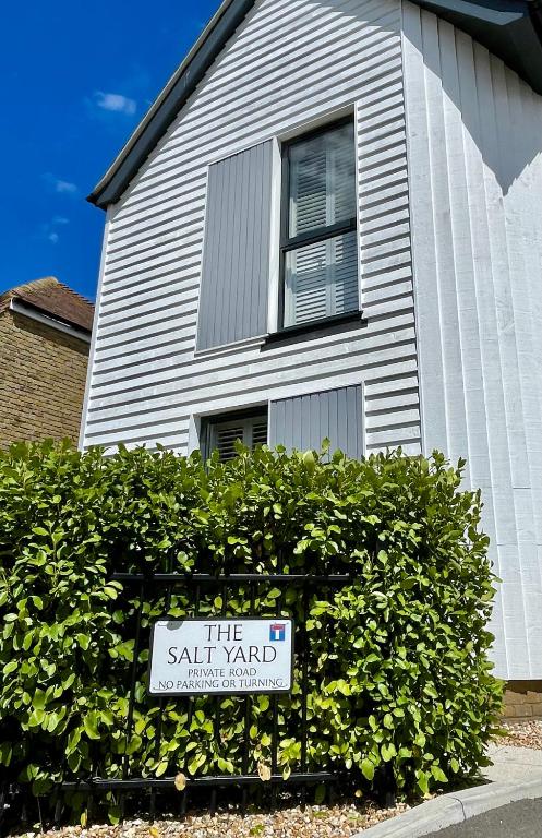 a white house with a sign in front of a bush at 3 The Salt Yard, Whitstable - free parking, centre of town, 2 min walk to beach in Whitstable