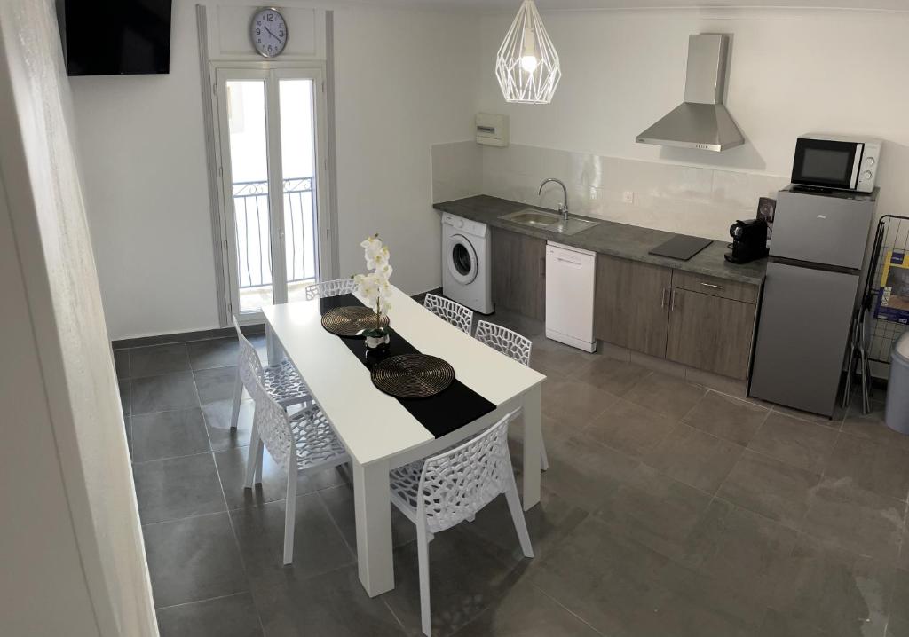 La cuisine est équipée d'une table et de chaises blanches ainsi que d'un réfrigérateur. dans l'établissement Appartement duplex plein cœur village, à Sérignan