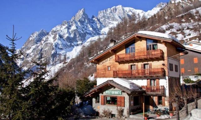 a large wooden building with snow covered mountains in the background at Hotel Chalet Joli in Courmayeur