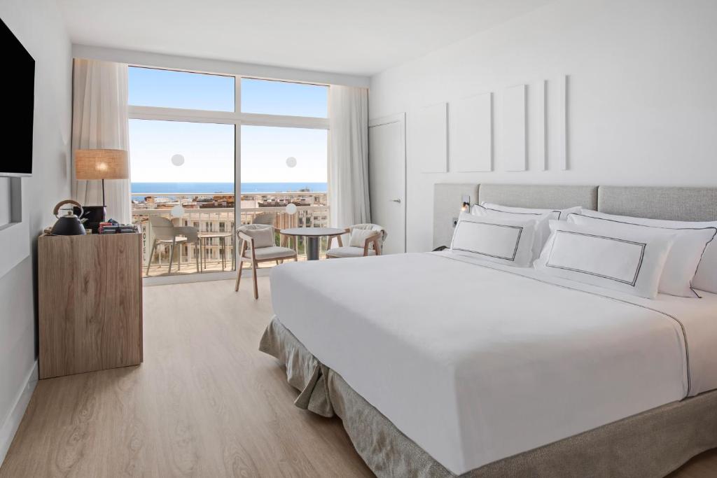 a white bedroom with a large white bed and a table at Meliá Lloret de Mar in Lloret de Mar