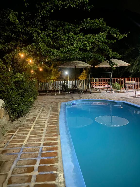 Una piscina azul por la noche con mesas y sombrillas. en Cabañas Between Hills, en San Alfonso