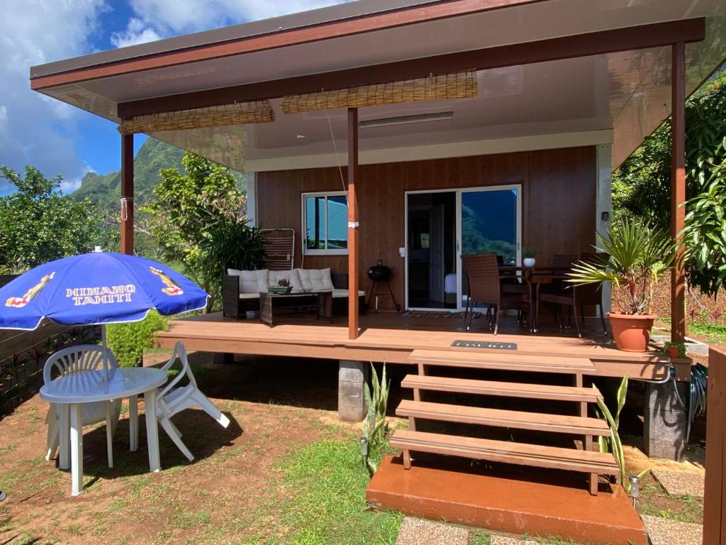 a house with a large wooden deck with a blue umbrella at Fare Maraea in Moorea