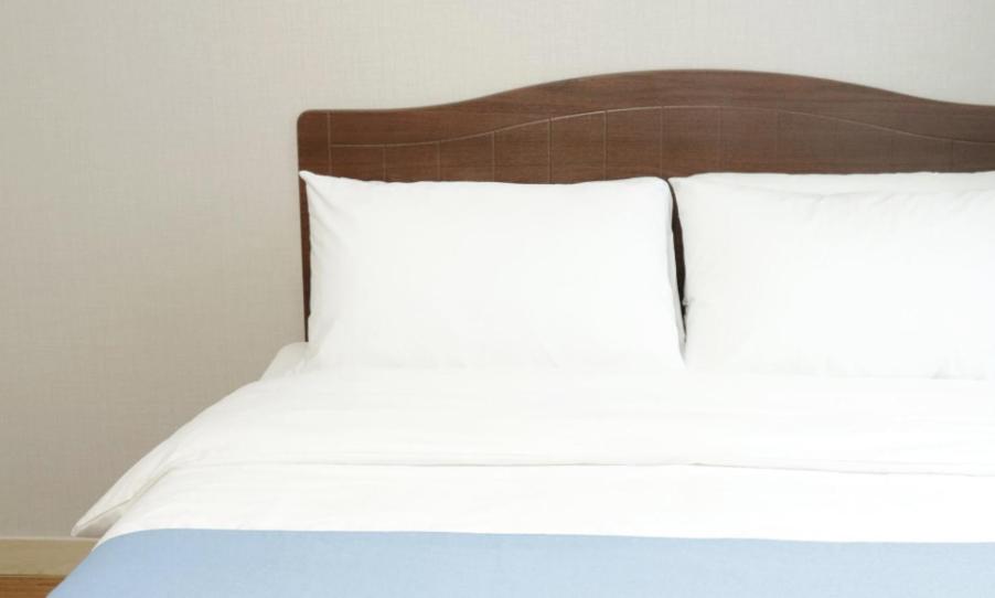 a bed with two white pillows and a wooden headboard at Jeju Orastay Hotel in Jeju