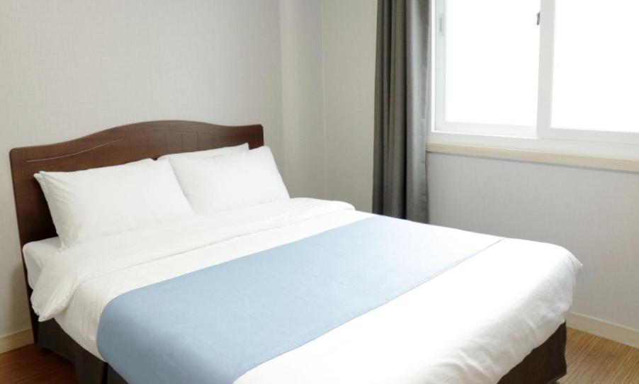 a large bed with white sheets and a window at Jeju Orastay Hotel in Jeju
