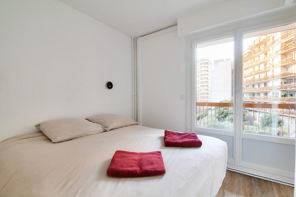 - un lit blanc avec 2 oreillers rouges dans une chambre avec fenêtre dans l'établissement Charmant appartement Paris, à Paris