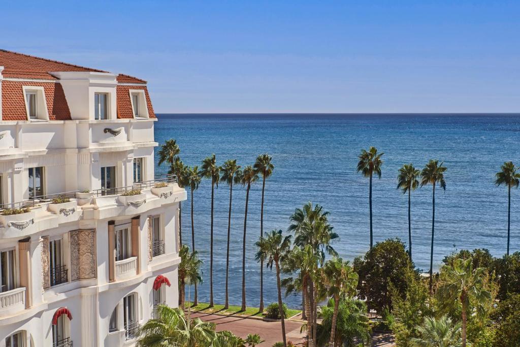 a building with palm trees and the ocean in the background at Hôtel Barrière Le Majestic Cannes in Cannes