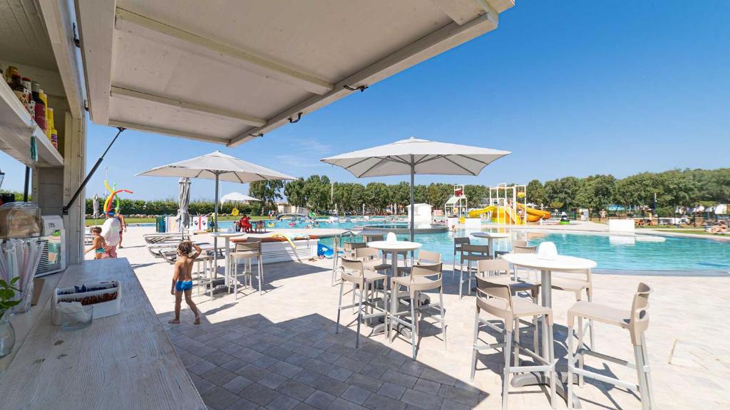 dziecko stojące przed basenem ze stołami i parasolami w obiekcie Camping Village Laguna Blu w mieście Fertilia