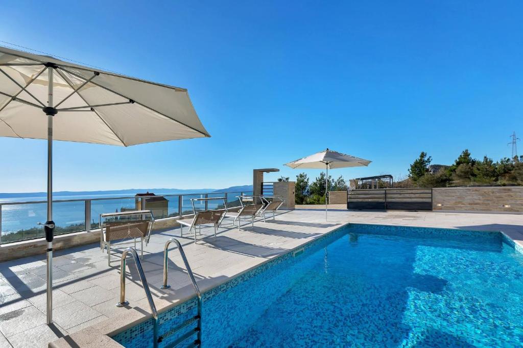 a swimming pool with chairs and an umbrella and the ocean at Villa Infinite in Makarska