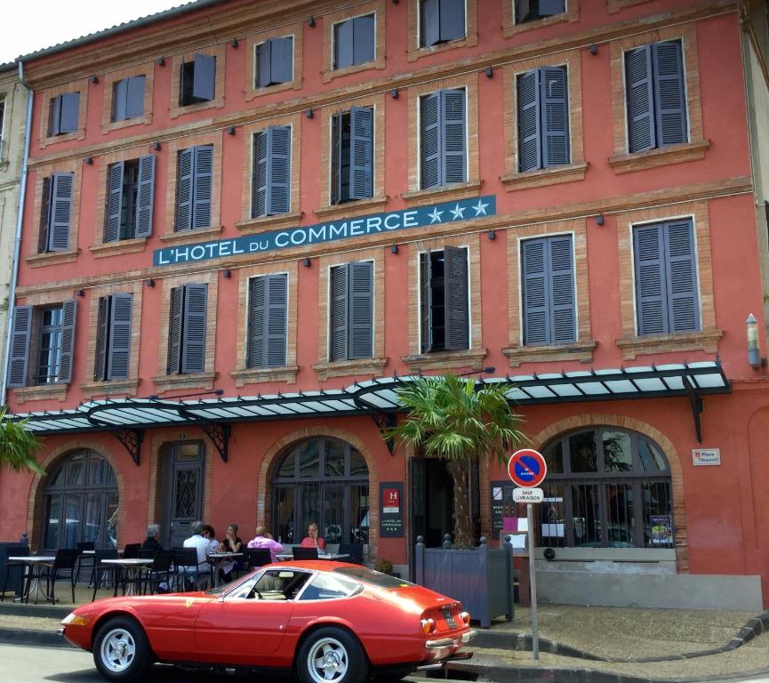 een rode auto geparkeerd voor een gebouw bij Hôtel du Commerce in Montauban