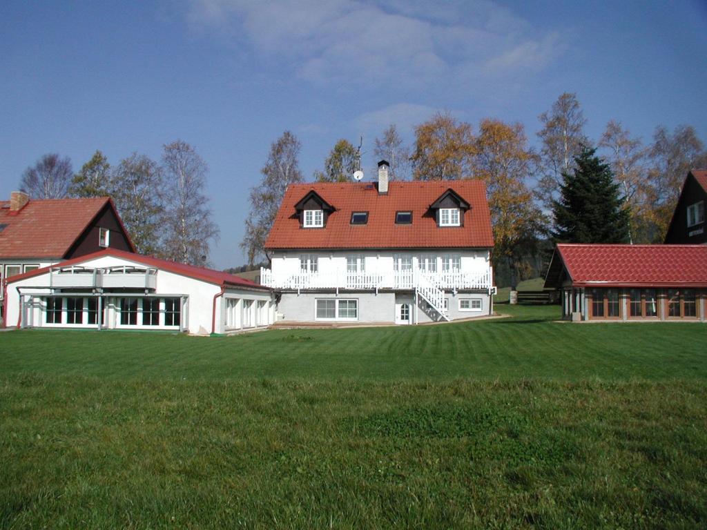 a large white house with a red roof on a green field at Pension Kohler in Deštné v Orlických horách