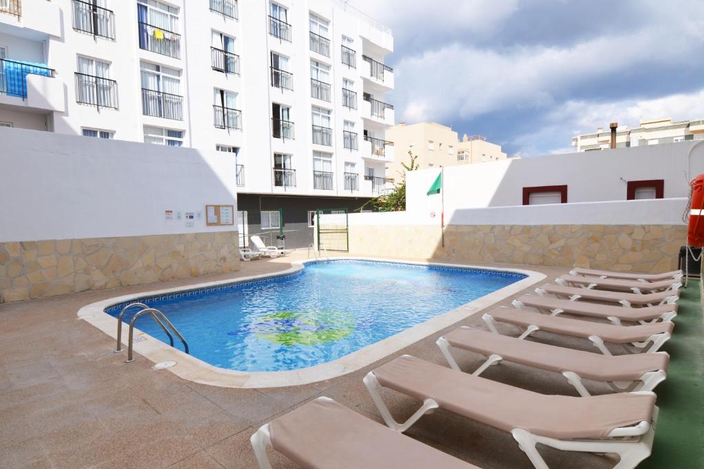 a swimming pool with lounge chairs next to a building at Vibra Calima Apartamentos - Adults only in San Antonio