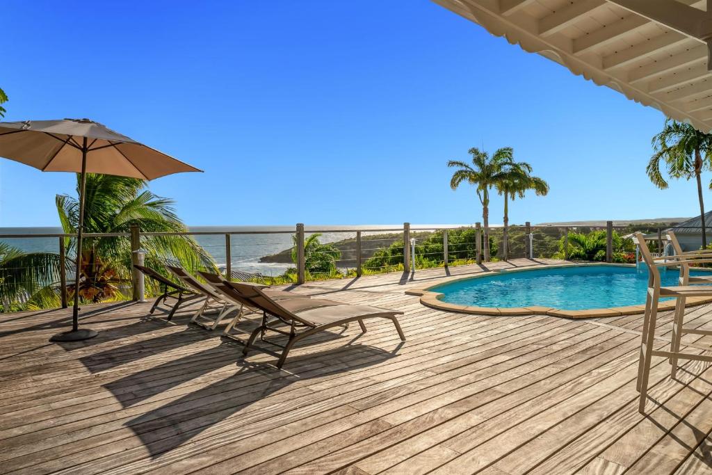 een terras met een zwembad en stoelen en een parasol bij Villa Alexandra in Saint-François