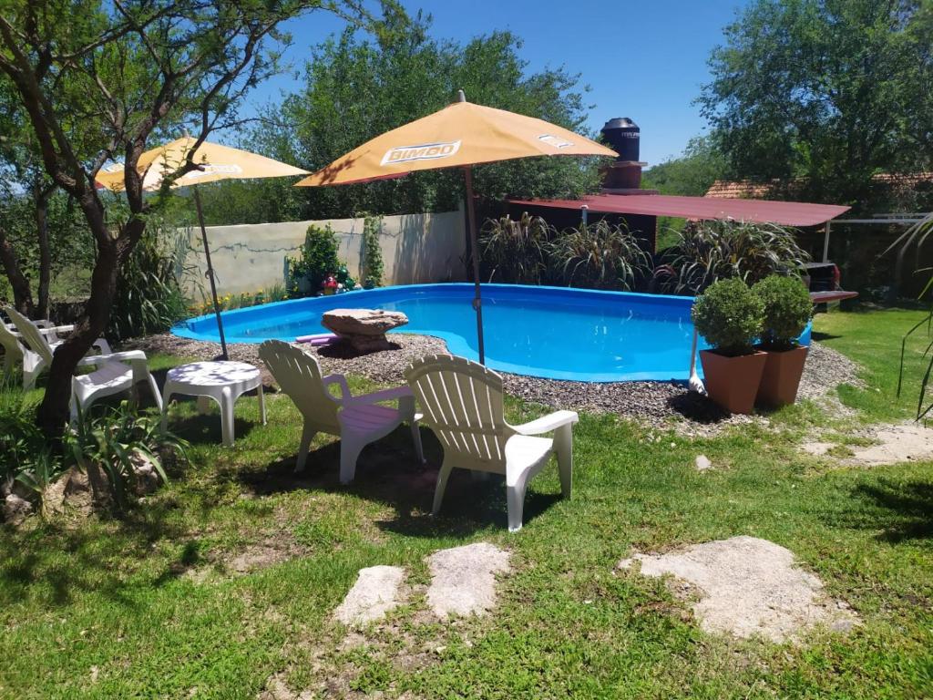 a yard with chairs and an umbrella and a pool at Cabaña con piscina compartida in Mina Clavero