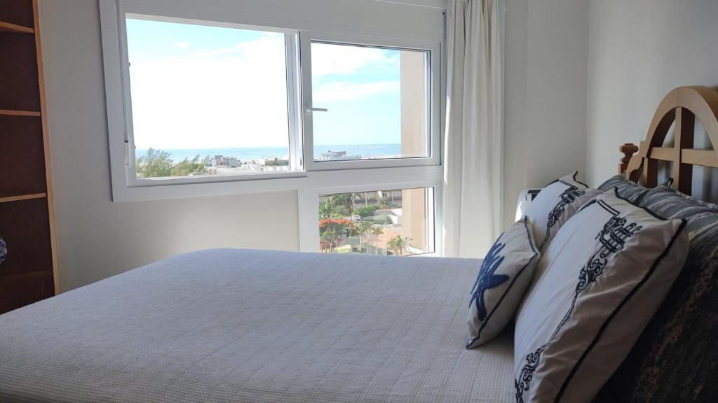 Un dormitorio blanco con una cama con dos ventanas. en Apto Torres com vista para o Mar, 3 suítes, sacada com churrasqueira, en Torres