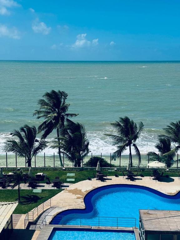a swimming pool with palm trees and the ocean at Cobertura Duplex Pé na Areia 509 Tabatinga Residence in Conde