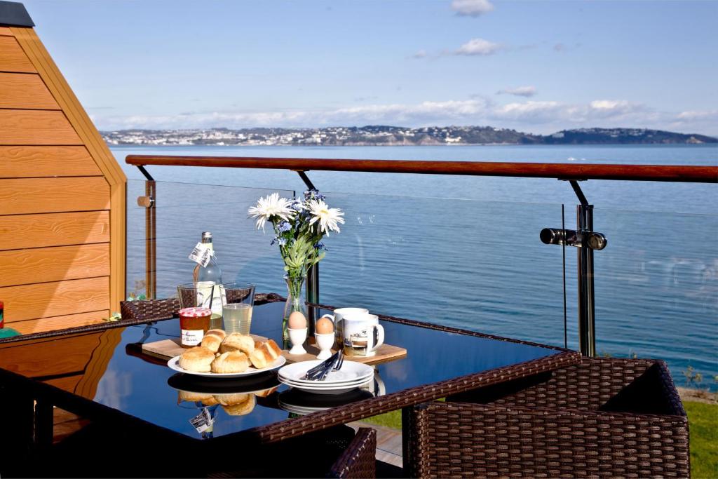 a table with food on a balcony with a view of the water at Avocet 2 Luxury Apartment with Pool and Parking in Brixham