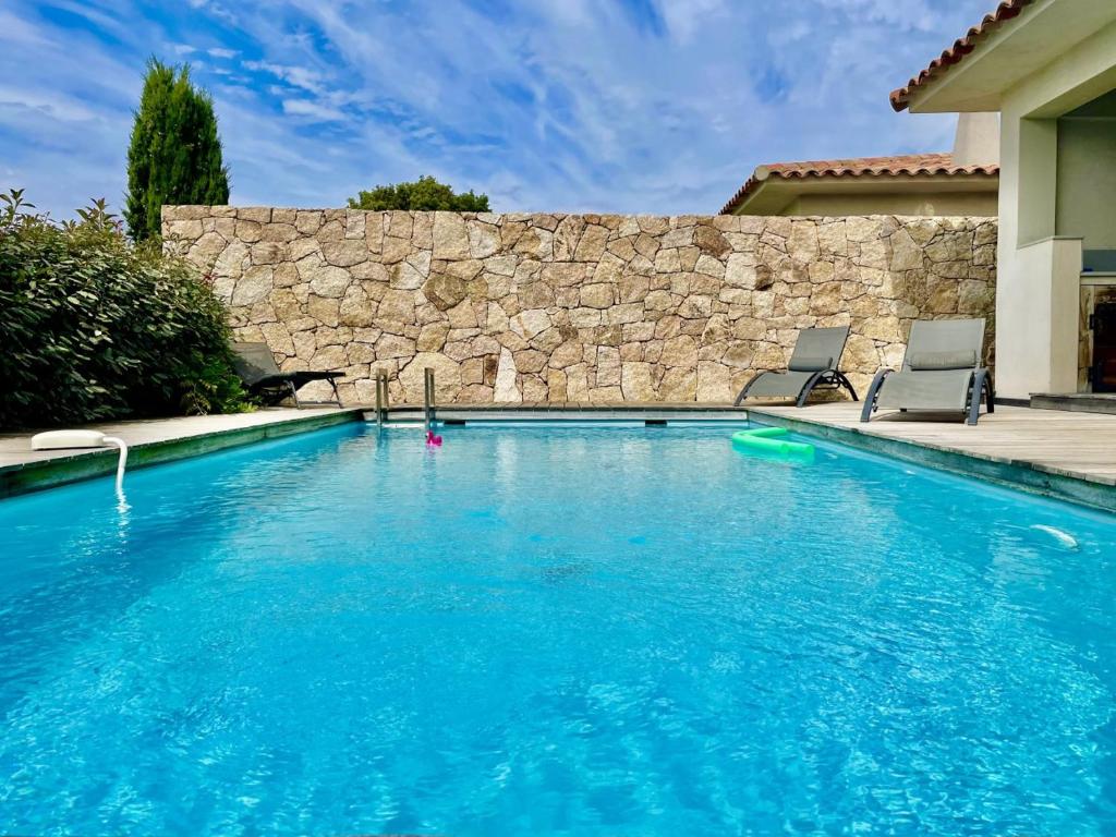 a swimming pool with two chairs and a stone wall at Villa Mare piscine et spa in Zonza