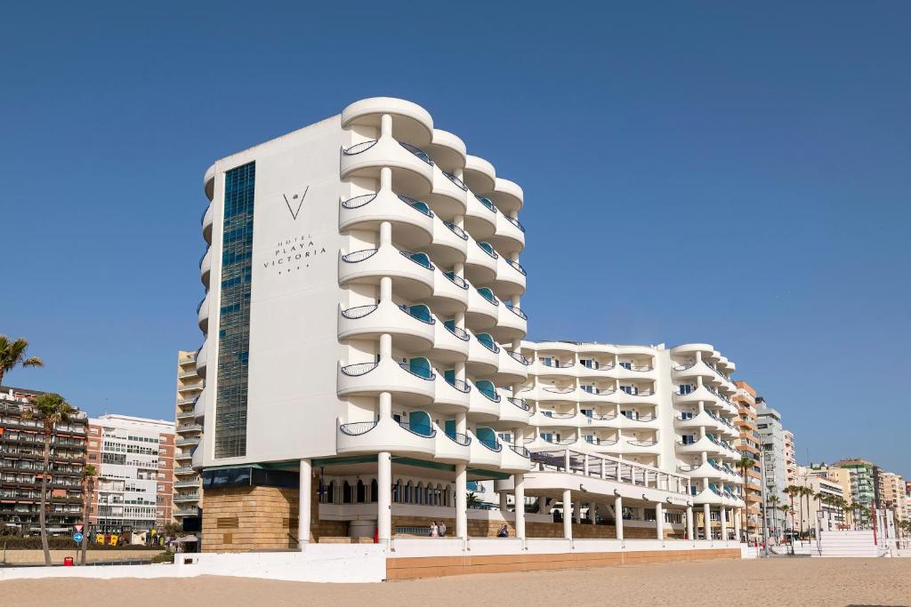 a white building on the beach with buildings at Hotel Playa Victoria in Cádiz